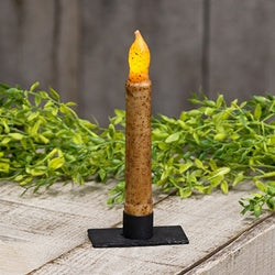 Iron rectangle candle holder holding battery operated ivory taper with greenery in the background