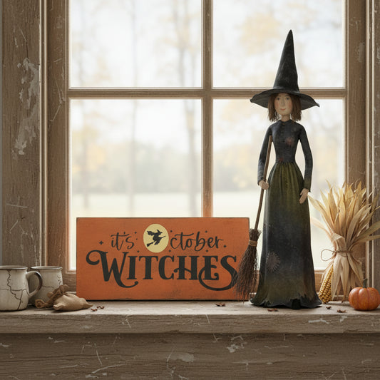 It's October Witches sign on a window sill with a witch figurine and a pumpkin.