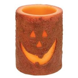 A battery-operated pillar candle with a jack-o'-lantern design, featuring a brown wax coating with a carved face and cinnamon dust.