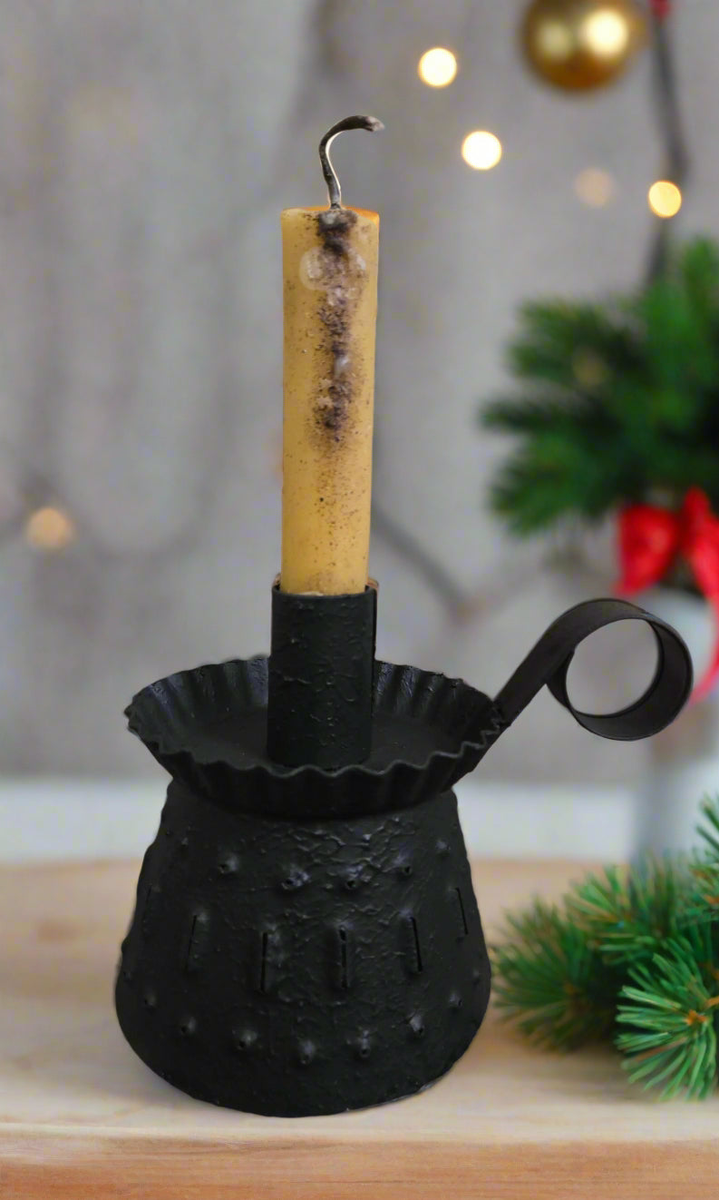 Black metal candle holder with a yellow candle on a wooden surface, Christmas decorations in the background.