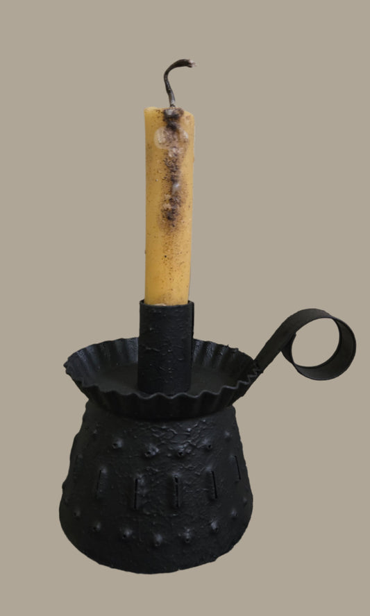 A textured black candle holder with a candle on top, designed with a handle and patterned surface.