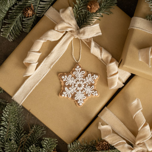 Gift wrapped in brown paper with a snowflake ornament and ribbons, surrounded by greenery.