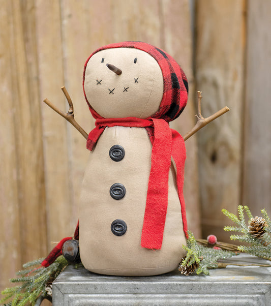 A beige-colored snowman doll with a buffalo plaid hat and a red scarf, featuring a weighted bottom, stick arms, a stick nose, and stitched facial features, dressed with three black buttons on the stomach.