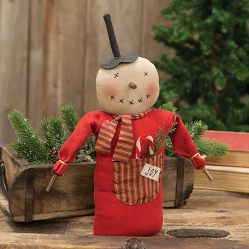 Snowman figure with a red outfit and 'JOY' label, standing next to a wooden cart with greenery, on a wooden surface.