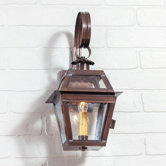 Primitive copper wall light with one light in copper finish on a white brick wall.