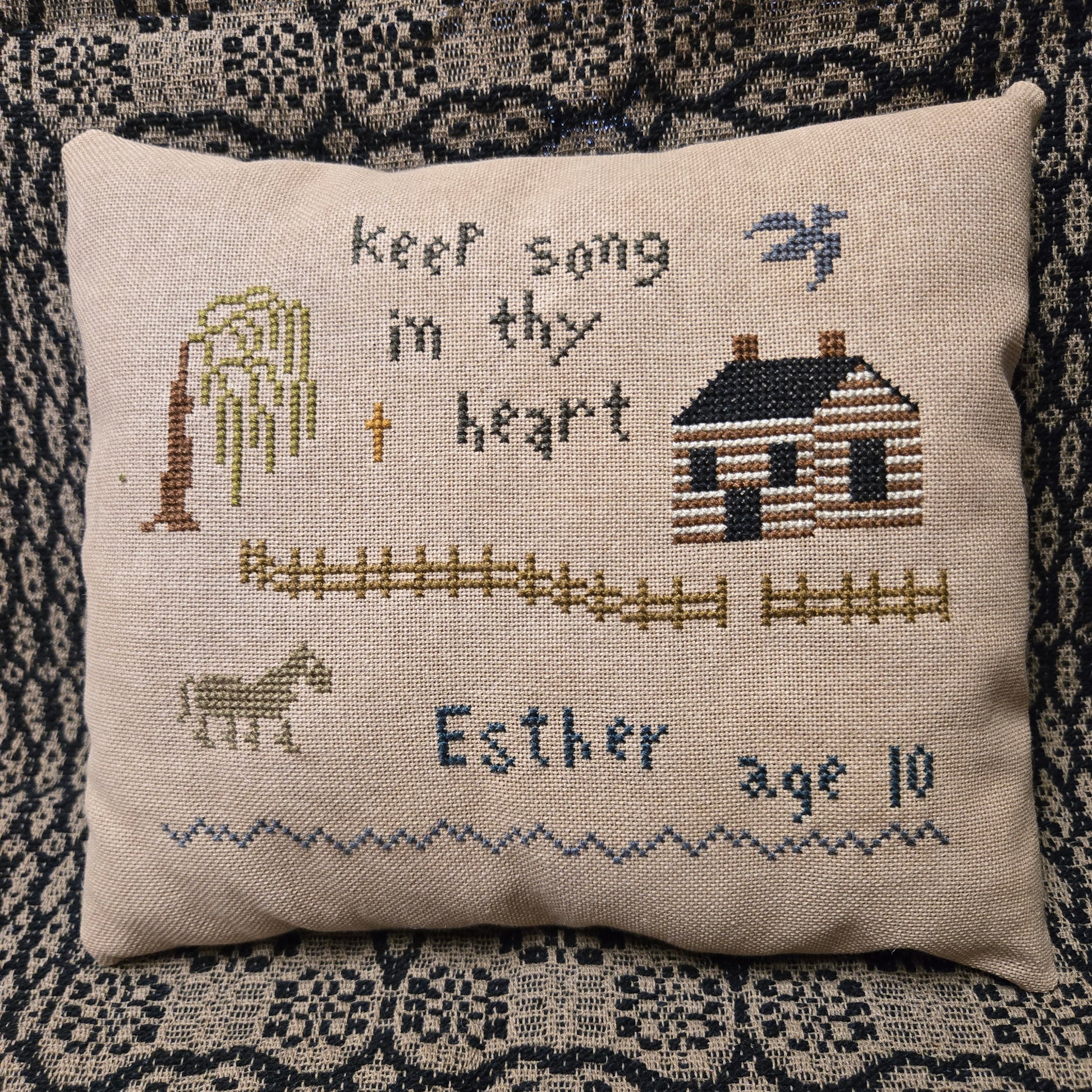 Decorative pillow with cross-stitched design and text on a textured fabric background
