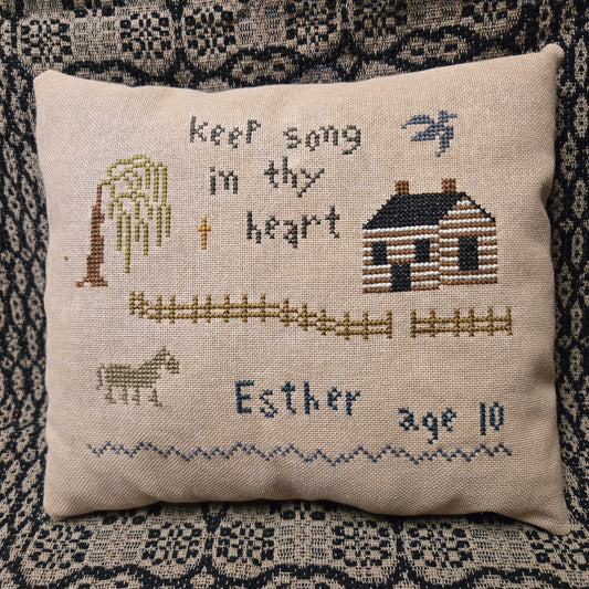 Decorative pillow with cross-stitched design and text on a textured fabric background