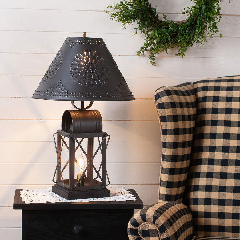 Decorative table lamp with black shade on a side table next to a plaid chair.