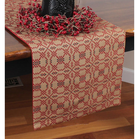 A red and black jacquard table runner with floral patterns, displayed on a wooden table with a decorative piece on top.