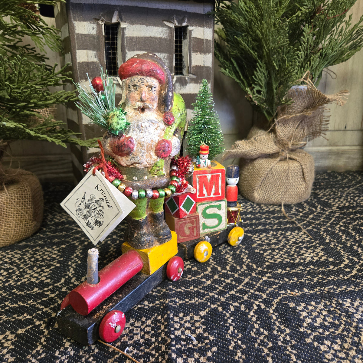 Chalkware santa standing on a toy train in front of a log cabin.