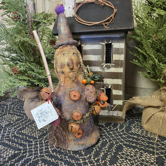 A handcrafted chalkware decoration depicting a whimsical witch with pumpkins and a broom, intended for Halloween decoration.