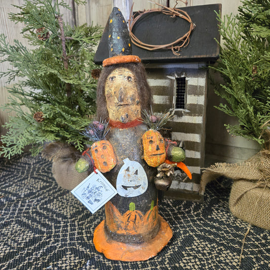 A handcrafted figurine of a witch with pumpkins, intended as Halloween decor.