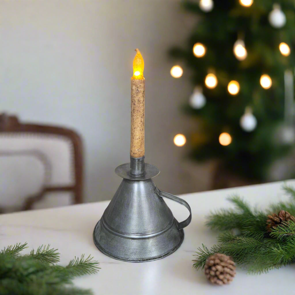 Metal candle holder with a lit candle on a table with Christmas decorations.