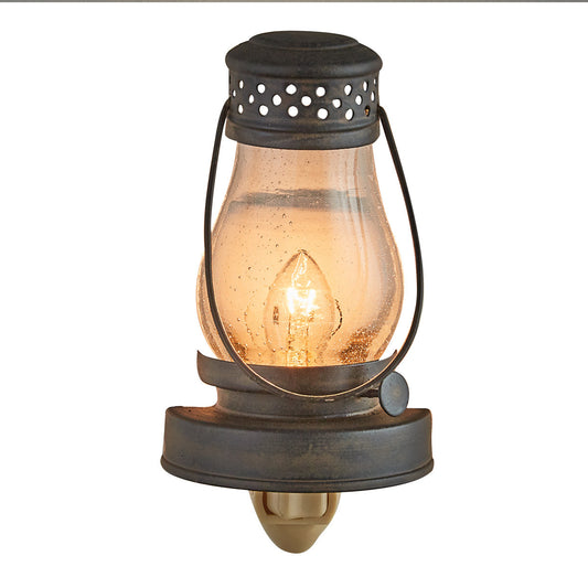 A metal lantern-style night light with a glass diffuser and a lit candle inside, providing a warm glow.