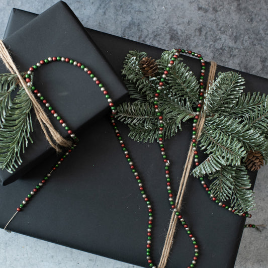 A garland of red, green, and silver beads tied together with twine, displayed on a black background.
