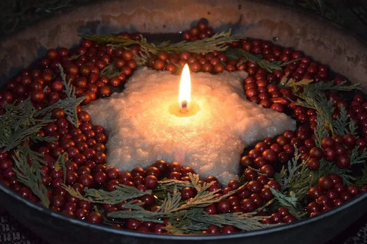 Candle surrounded by red berries and greenery in a dark setting