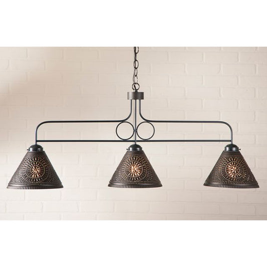 Black chandelier with three textured lampshades against a white brick wall.