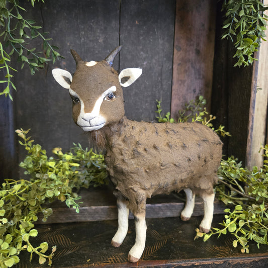 Decorative goat on a wooden background with greenery
