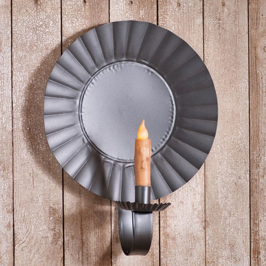 A smokey black large round candle sconce with a crimped edge bevel design, mounted on a wooden wall, with a candle in the center.