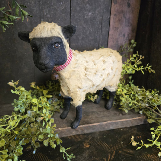 Sheep figurine with a red checkered scarf on a wooden surface with greenery
