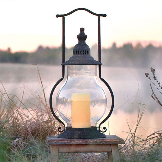 Lantern with candle inside on a wooden stand in front of a lake scene