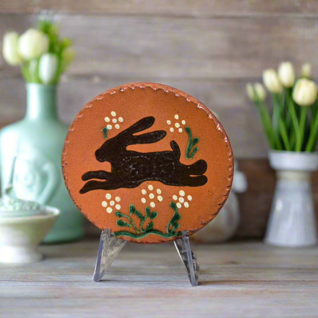 Round redware plate with a bunny design on a textured surface