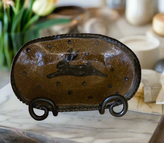 A medium oval stoneware plate with a brown glazed finish and a bunny and polka dot design