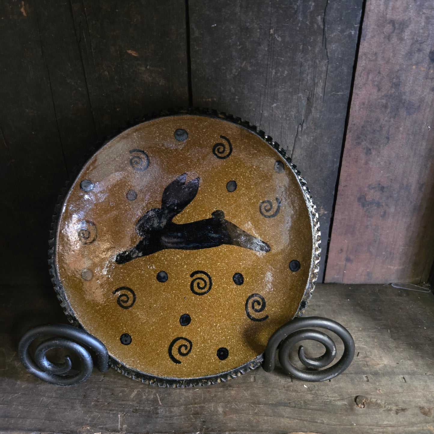 Decorative pottery piece with black silhouette and spiral patterns on a wooden background