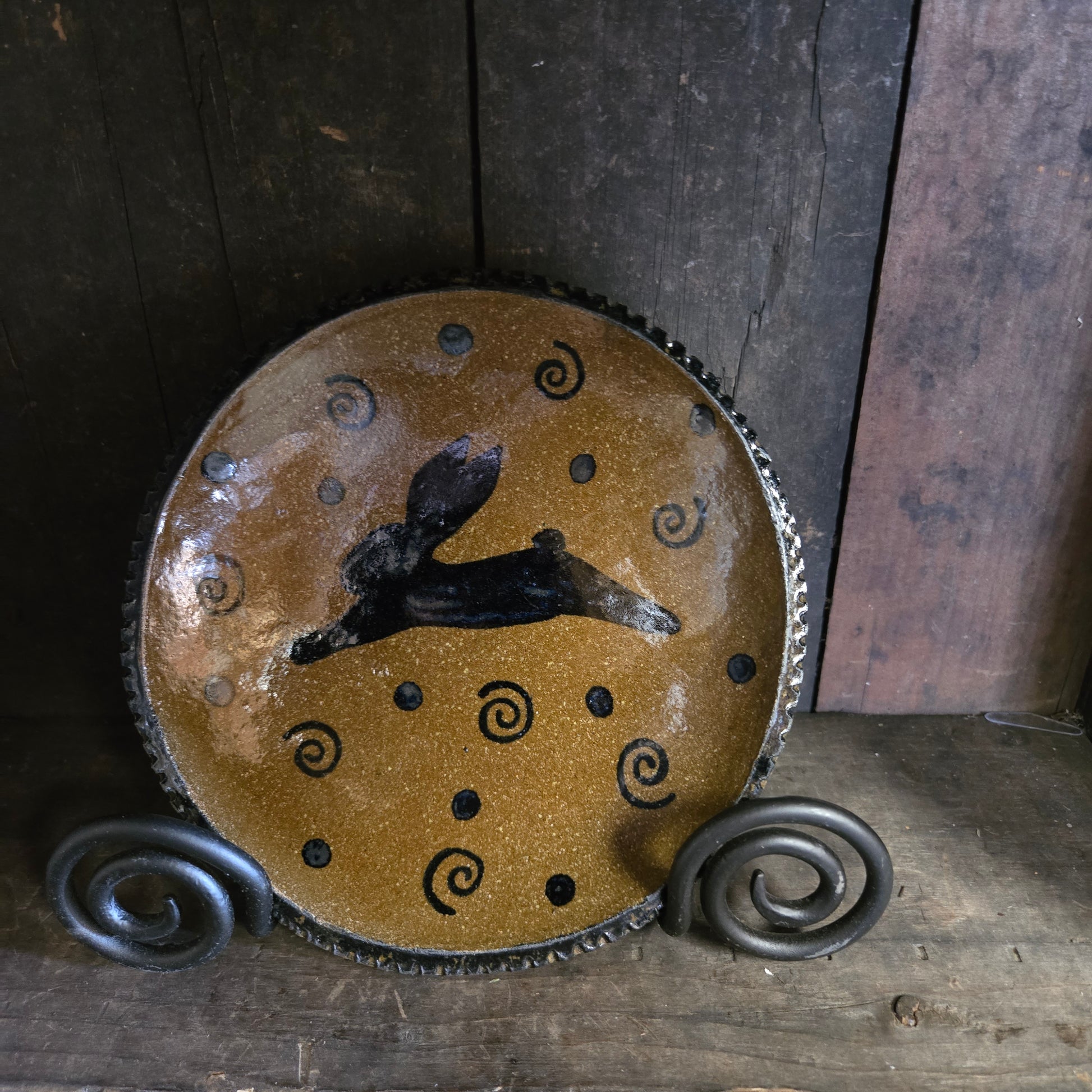 Decorative pottery piece with black silhouette and spiral patterns on a wooden background