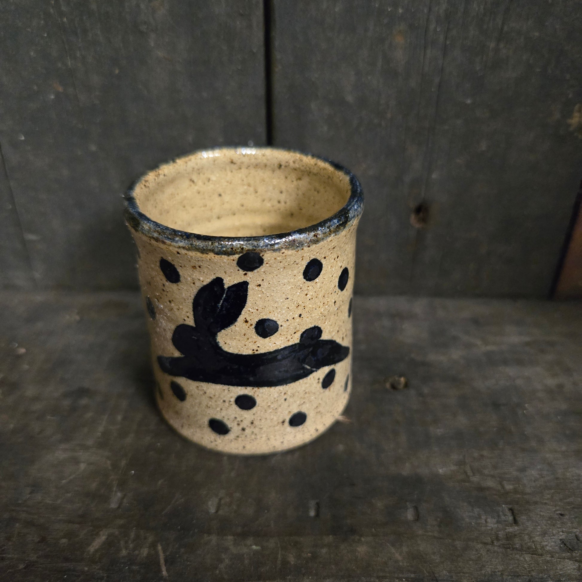 Cylindrical ceramic cup with black patterns on a dark wooden surface