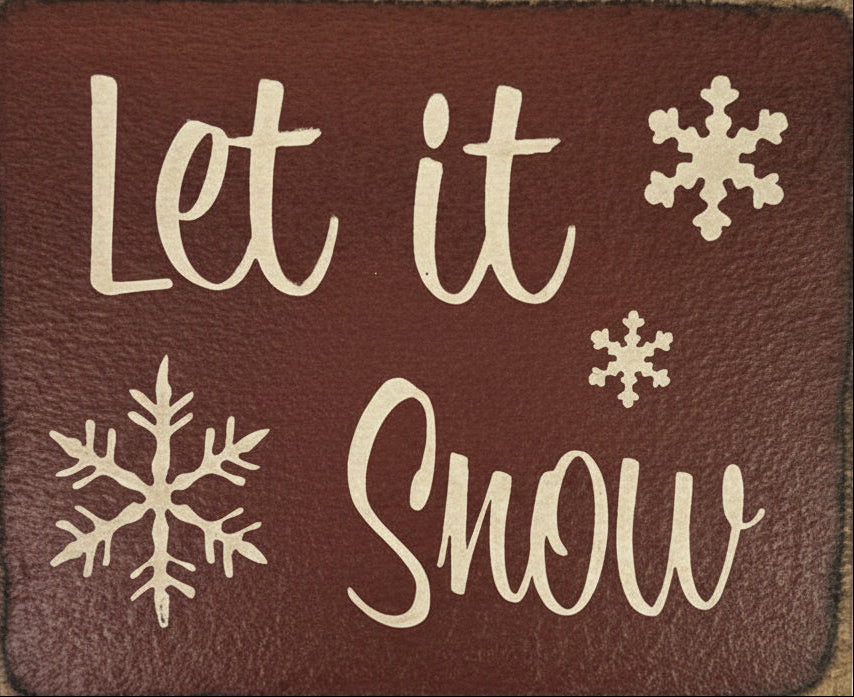 Decorative sign with 'Let it Snow' text and snowflake designs on a brown background