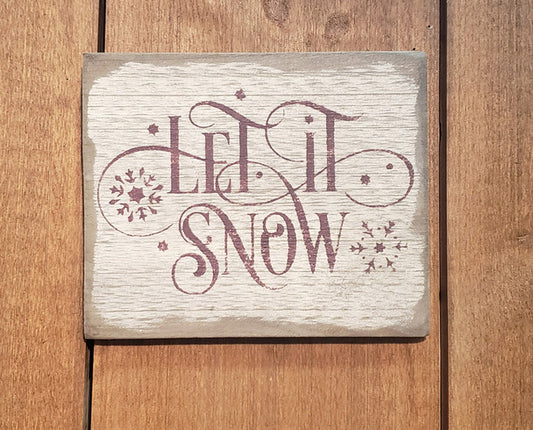 Weathered sign with the words "Let It Snow" and snowflakes on a wooden background