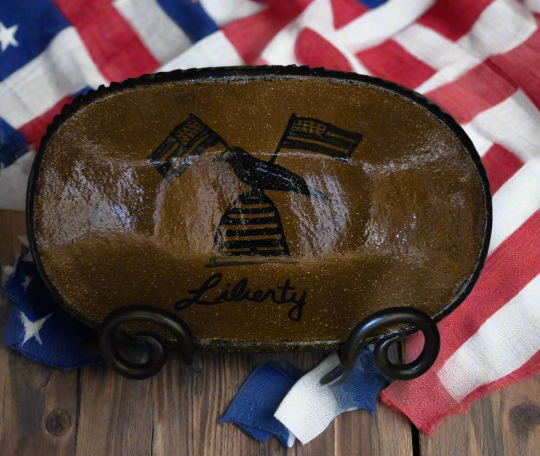 A medium oval stoneware plate with a brown glazed finish and a bee skep, crow and flag motive with the word 'Liberty'