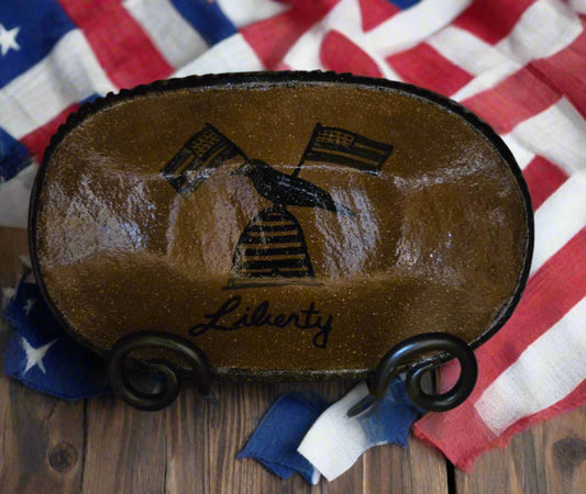 A medium oval stoneware plate with a brown glazed finish and a bee skep, crow and flag motive with the word 'Liberty'