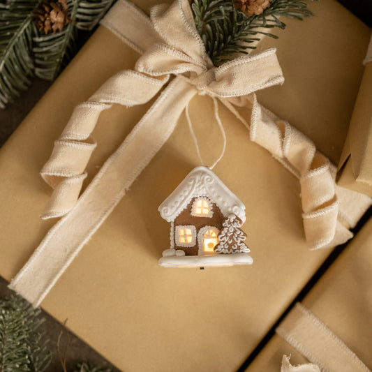 Decorative gingerbread house ornament on a wrapped gift with a beige ribbon.