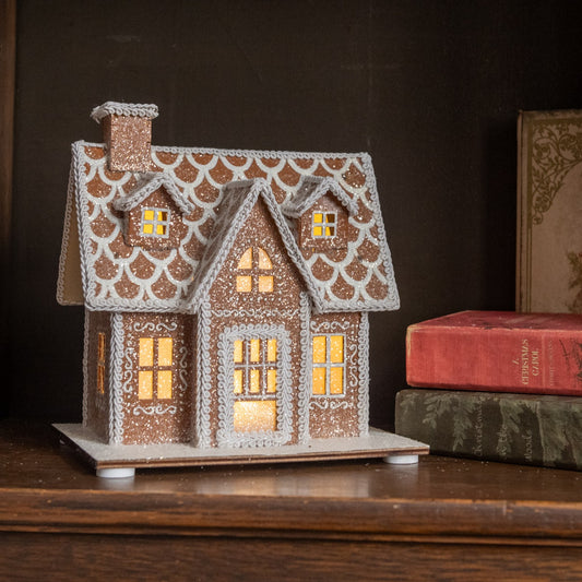Decorative gingerbread house with lit windows on a wooden surface.
