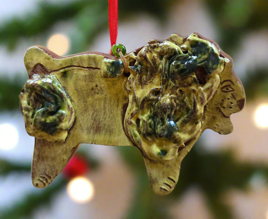 Redware lion ornament hanging on a red string with a blurred Christmas tree background.