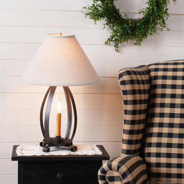 Lamp on a side table next to a plaid chair with a wreath on the wall.