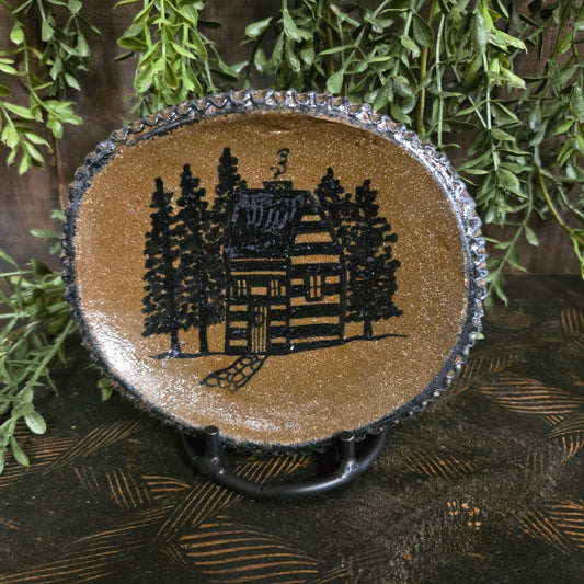 Decorative pottery with a black silhouette of a house on a brown background, surrounded by greenery.