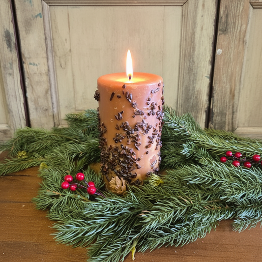 Candle with pine needles and berries on a wooden surface