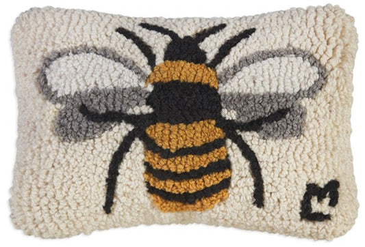 A hooked wool pillow with a design of a bee on a white background, with a velveteen backing.