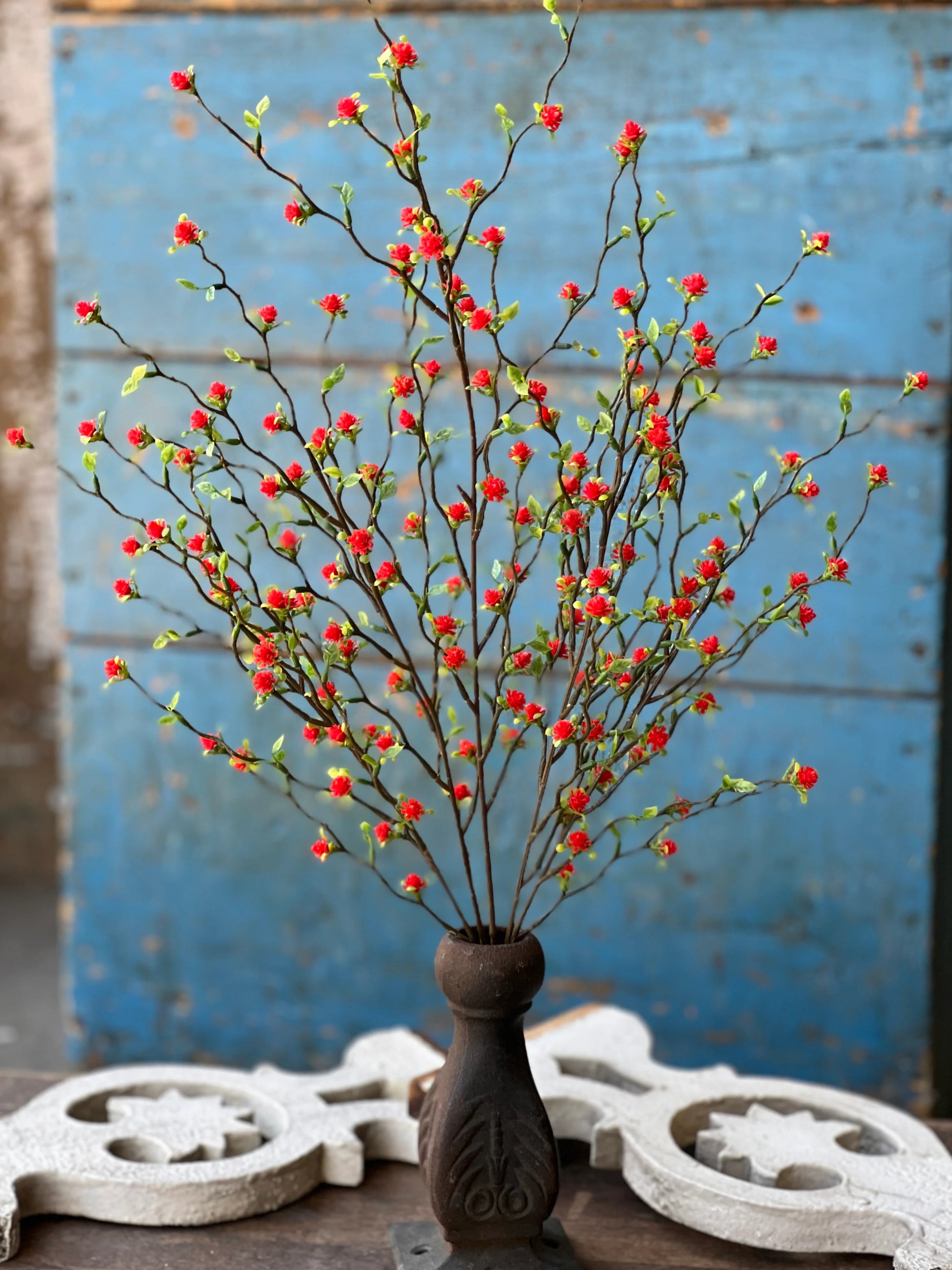 A faux floral bush with red berries in a brown vase, placed on a surface with a blue background.