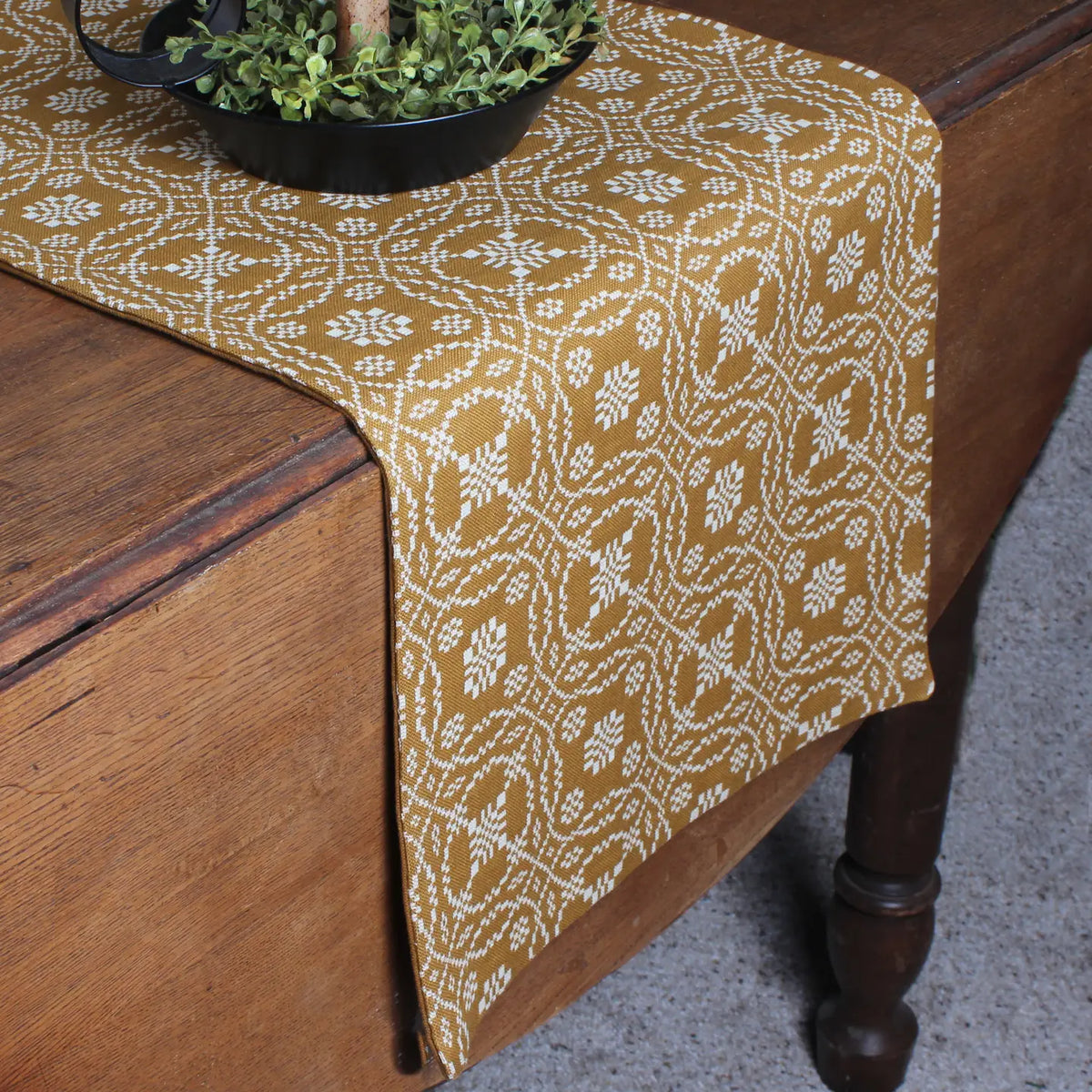 Patterned table runner on a wooden table with a plant.