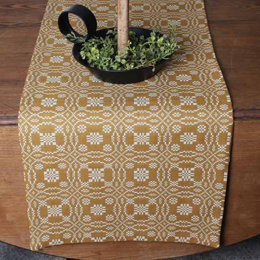 Patterned table runner on a wooden table with a black bowl of greenery.
