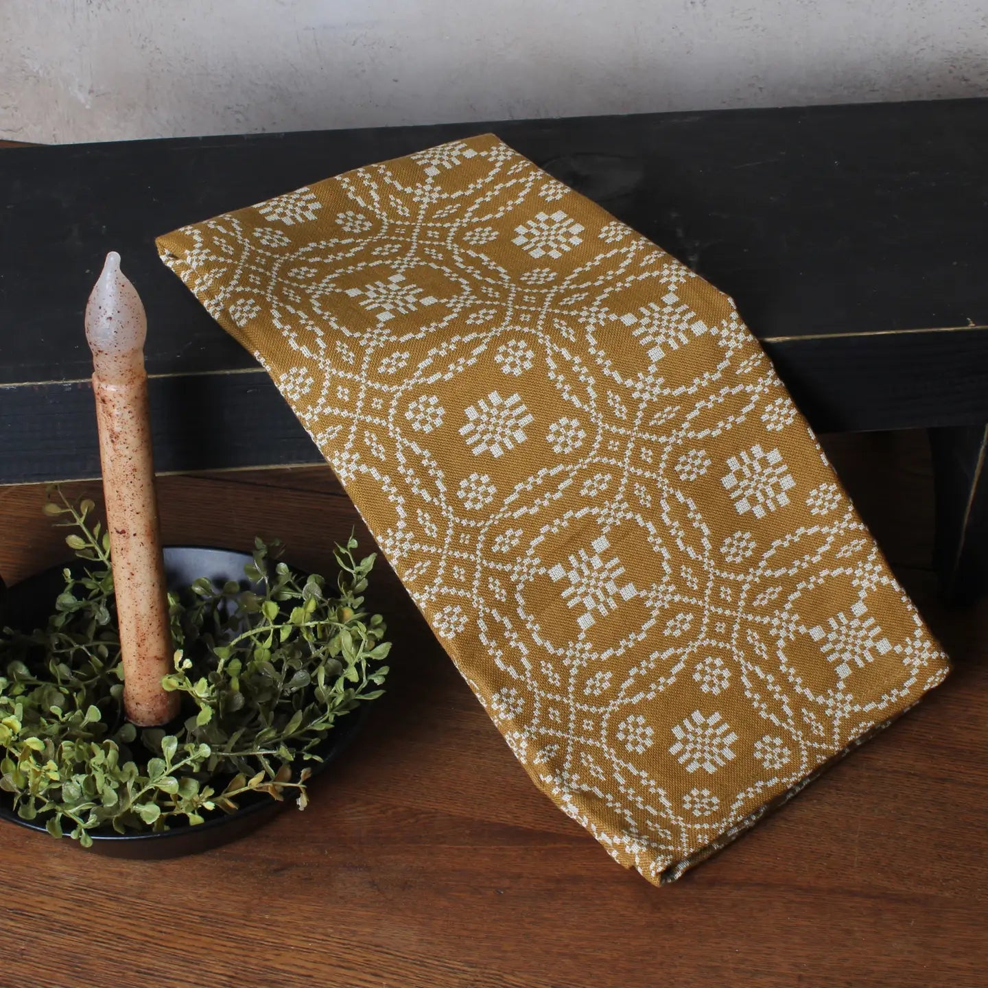Decorative table runner with floral pattern on a wooden surface with a candle and greenery.