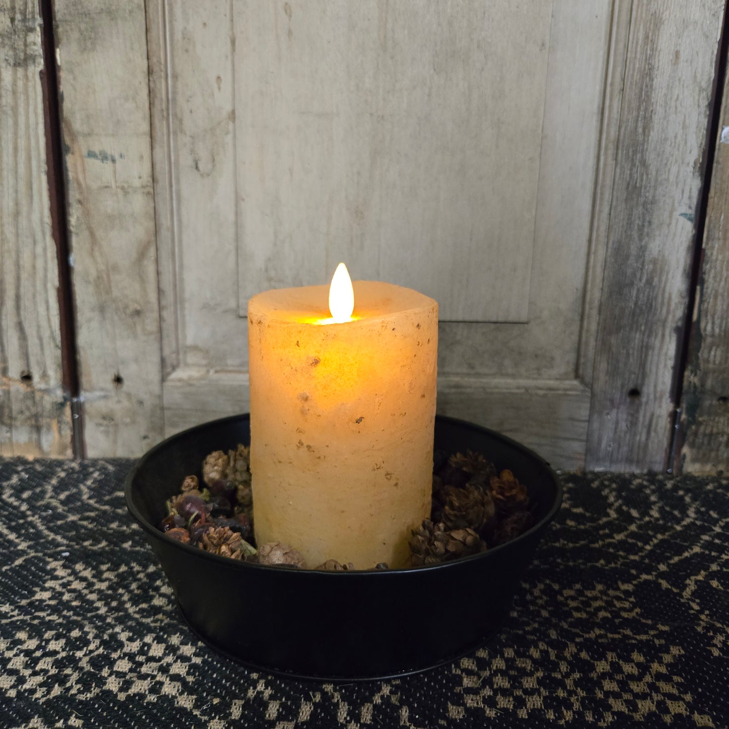 A 3 inch by 4 inch moving flame pillar candle in burnt ivory color, placed in a black holder with a timer feature.