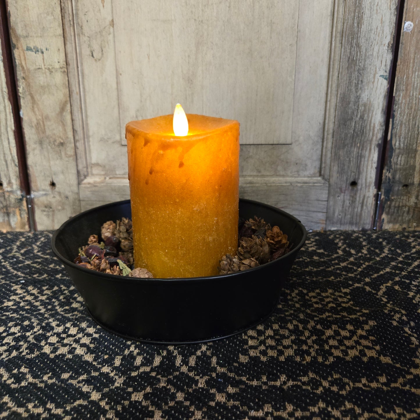 A synthetic moving flame pillar candle in mustard color displayed in a black holder with a timer feature.