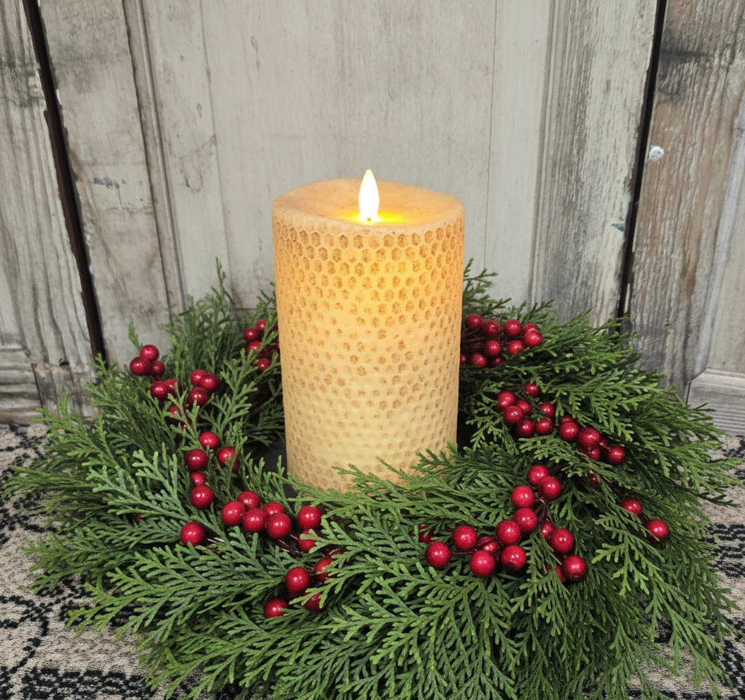 A 7-inch beeswax honeycomb pillar candle in burnt ivory color with a lit wick and a realistic moving flame, placed on a dark holder, surrounded by greenery.