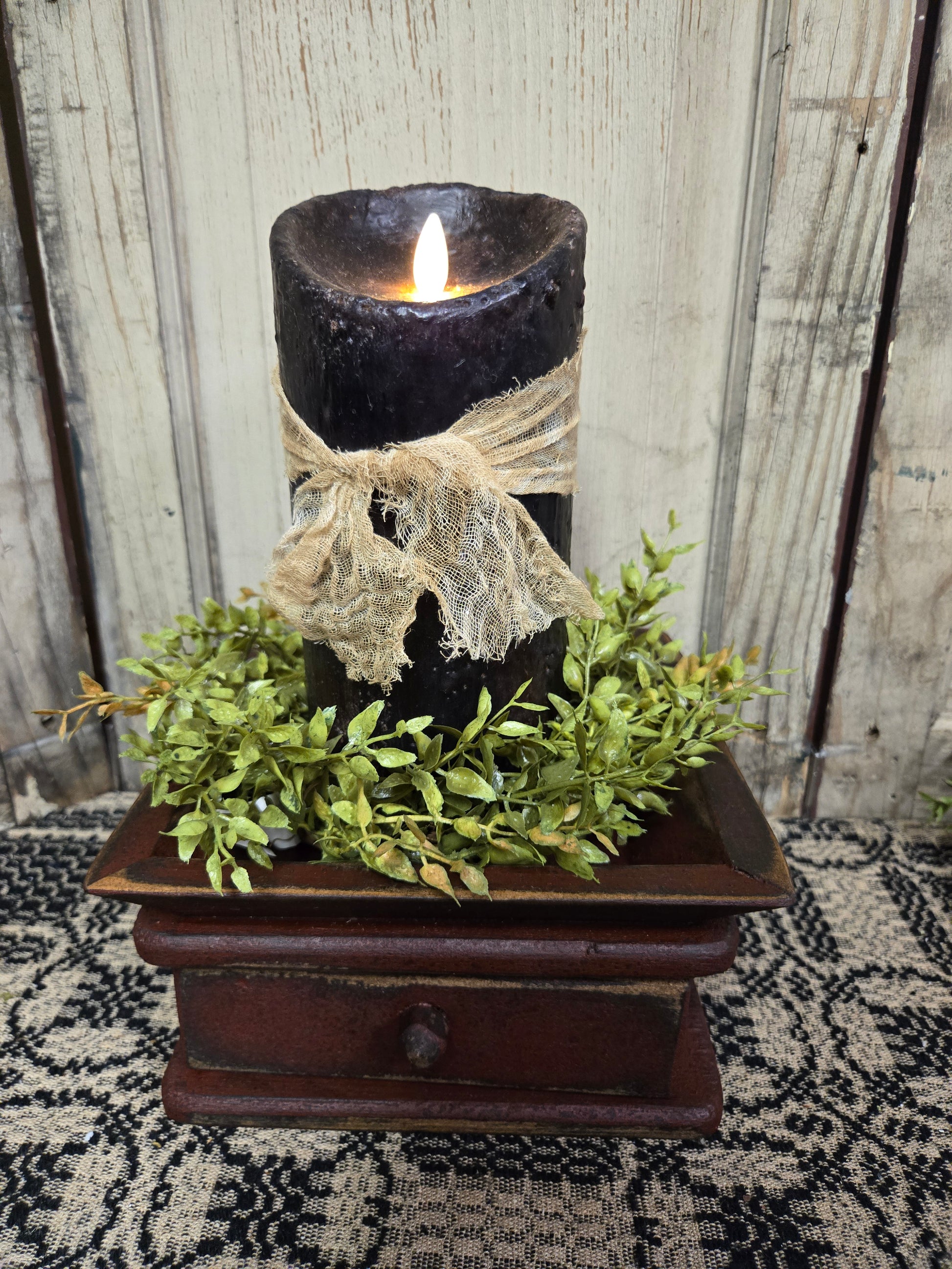 A black moving flame pillar candle with a realistic flame, placed on a wooden base with a cheesecloth fabric tie.