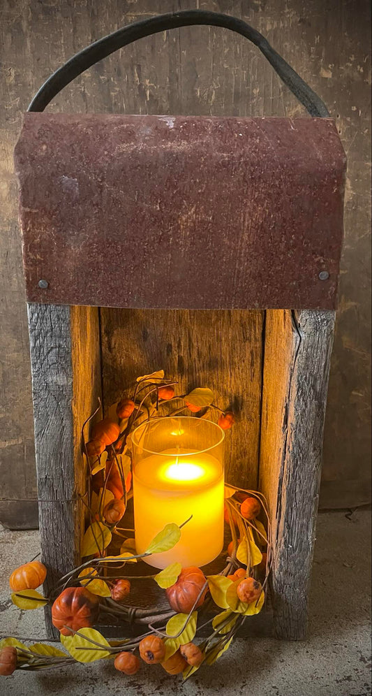 Wooden lantern with a lit candle inside, surrounded by autumn-themed decorations.